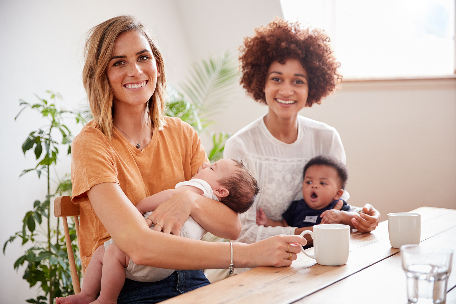 Two mothers and their babies, smiling and looking at the camera. They are clothed, showered and caffeinated, thanks to quality postpartum support and counseling in Tigard, OR 97223 