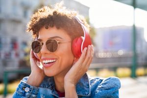Woman smiling and holding her headphones on, wearing sunglasses, after anxiety therapy in Tigard, OR. No more worry, feeling hopeful and confident. 97223