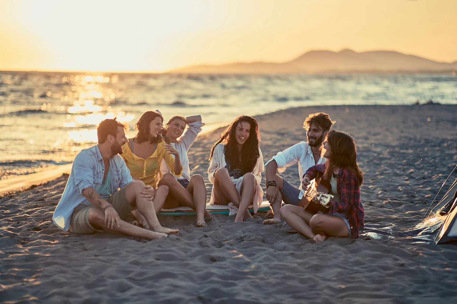 Group of smiling friends with guitar at beach. Relationship therapy in Tigard, OR helps solve relationship problems so you stay connected with friends and family.